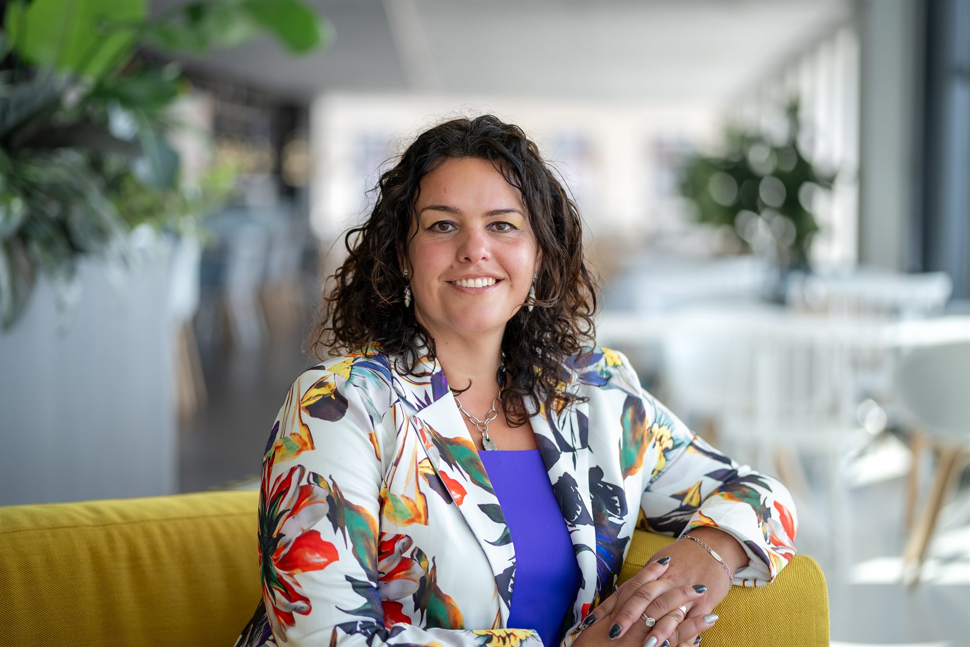 Zakelijke headshot van een glimlachende vrouw in een gekleurd pak in een kantooromgeving.
